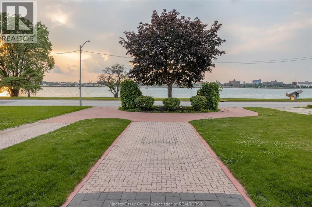 A walkway with a brick pattern leads to a tree in a grassy area.
