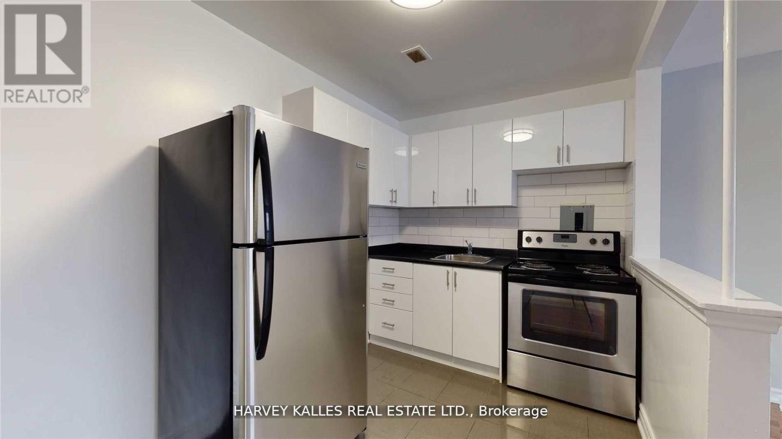 A kitchen with a black fridge, stove and white cabinets.