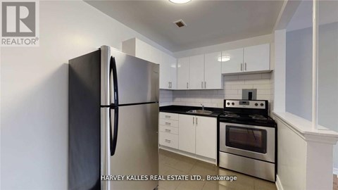 A kitchen with a black fridge, stove and white cabinets.