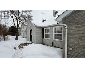 A house with a grey siding and a white door is surrounded by snow.
