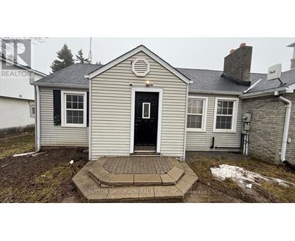 A house with a grey siding and a white door is surrounded by snow.