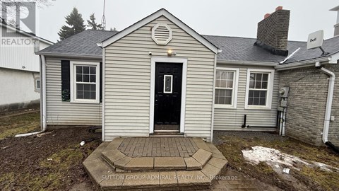 A house with a grey siding and a white door is surrounded by snow.
