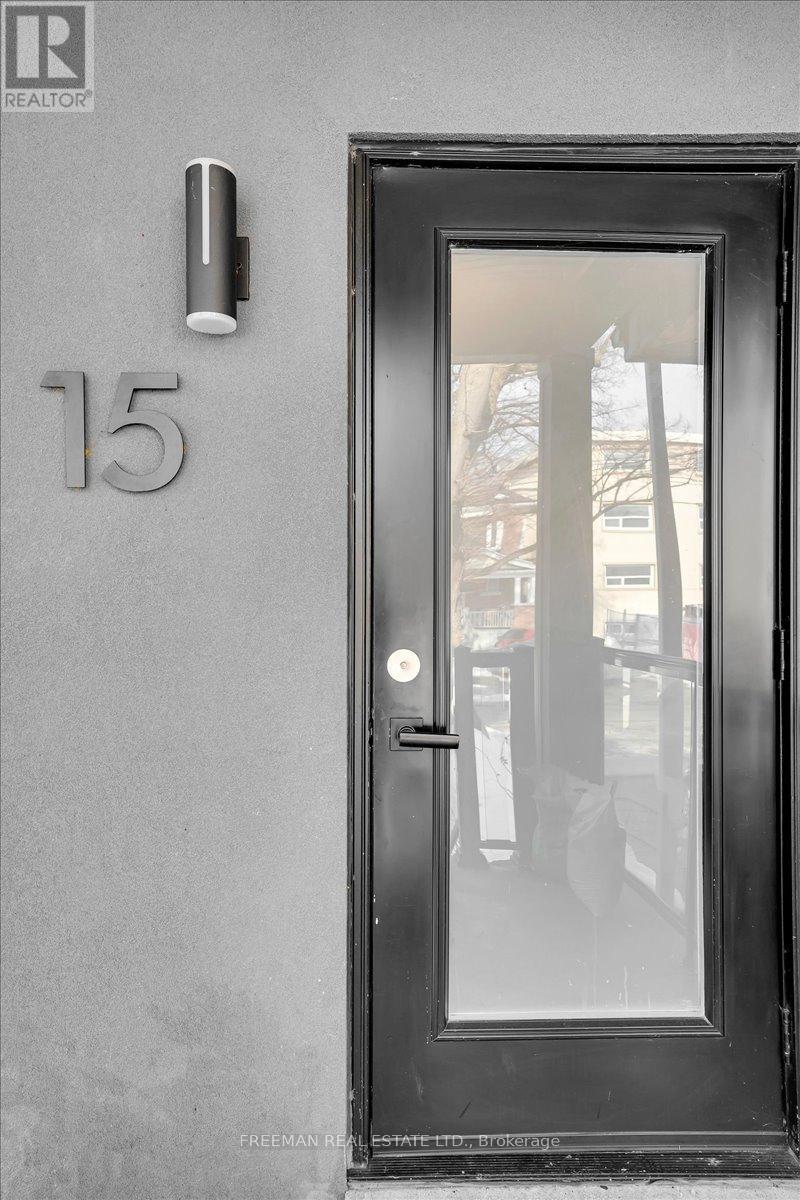 A black door with a glass window and a silver handle on a grey wall with the number 15 on it.
