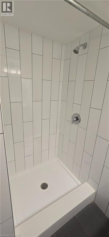 A white tiled shower with a drain in the middle.