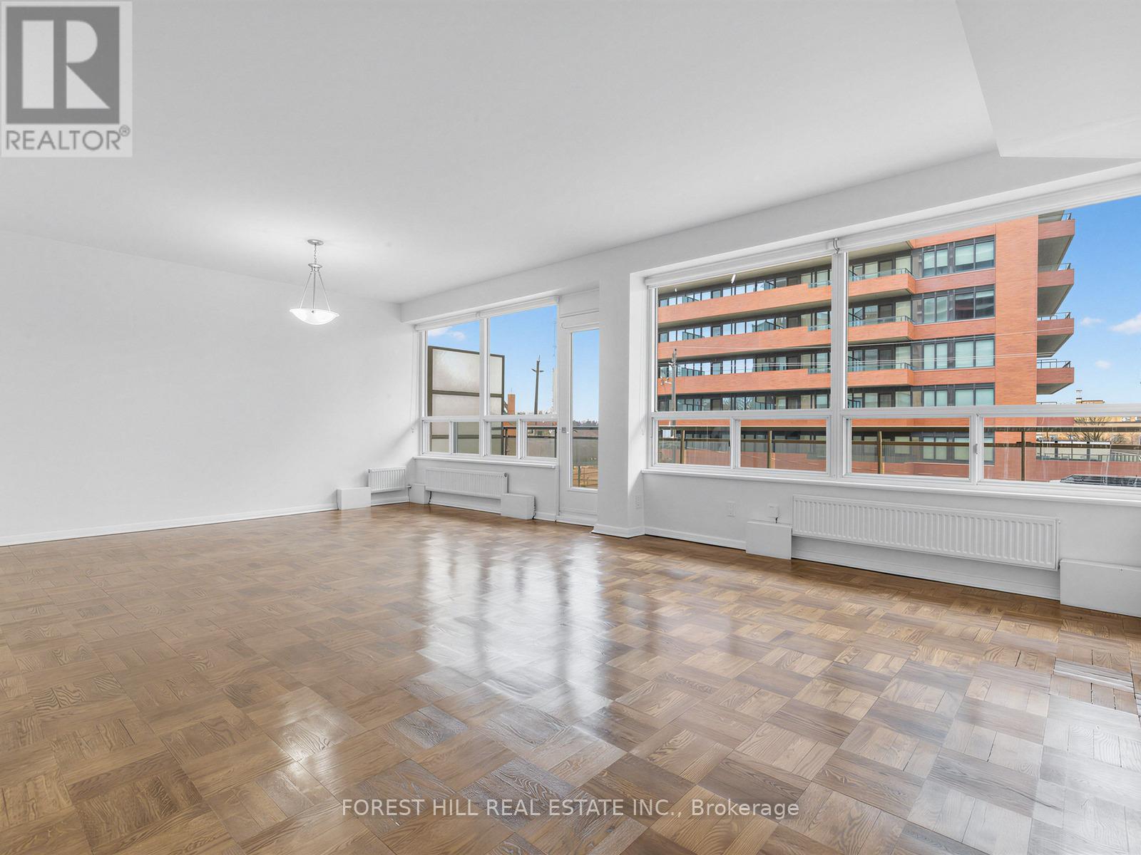 A spacious room with wooden flooring and a large window overlooking a building.