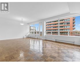 A spacious room with wooden flooring and a large window overlooking a building.
