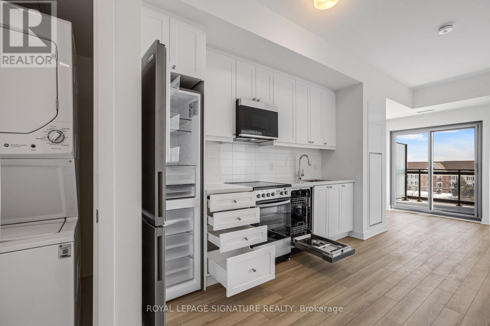 A modern kitchen with white cabinets and appliances, a refrigerator with its door open, and a view of the city through a large window.