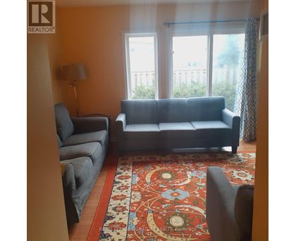 A living room with a grey couch, a grey chair, and a red patterned rug.