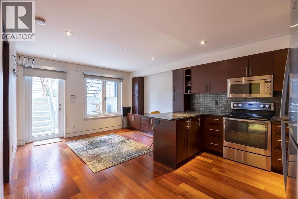 A modern kitchen with dark wood floors and stainless steel appliances.