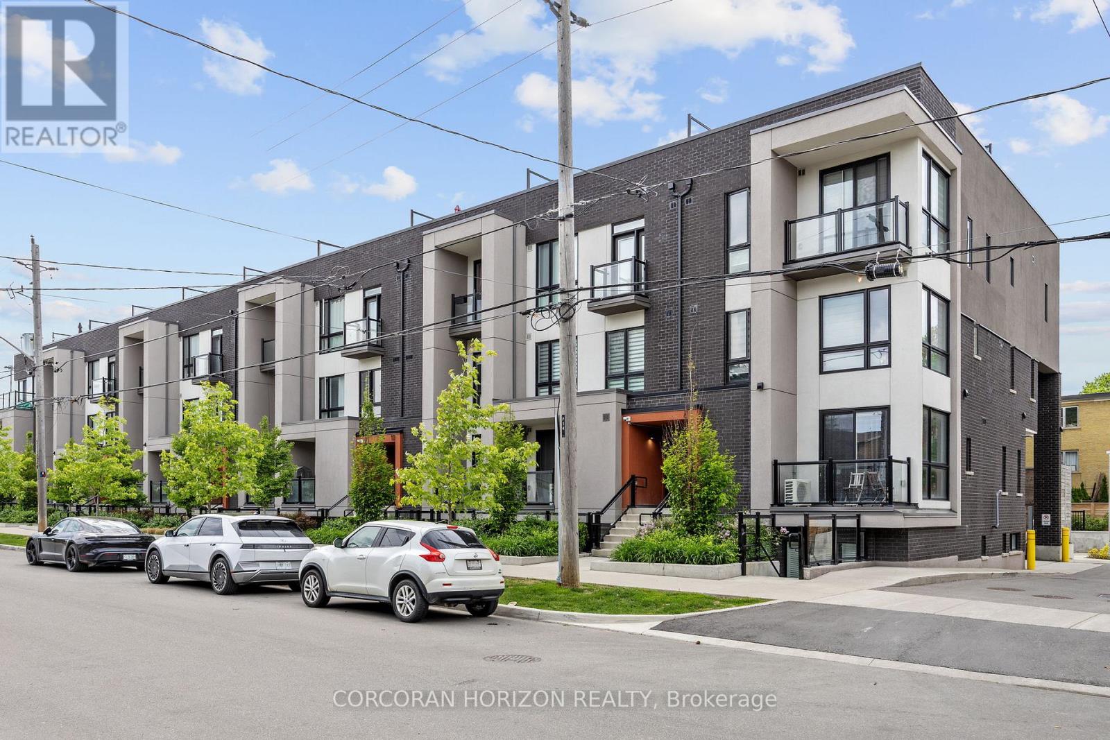 A row of modern townhouses with cars parked in front.