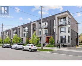 A row of modern townhouses with cars parked in front.
