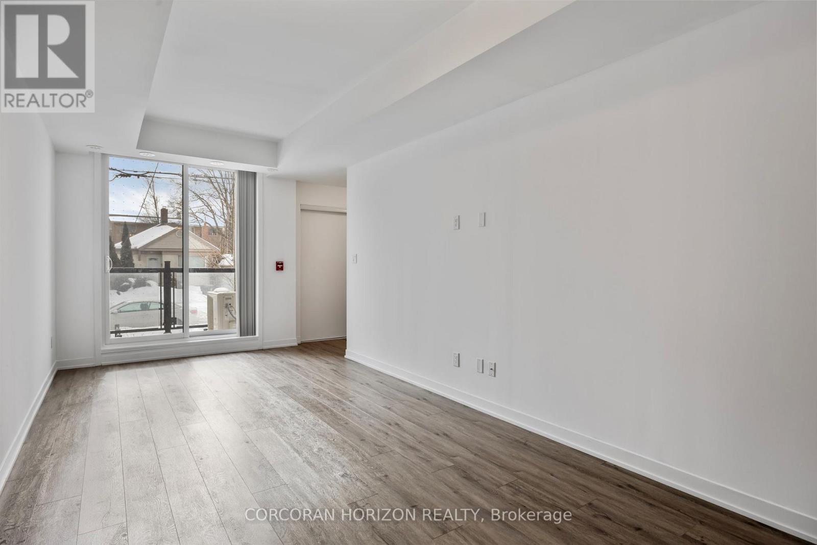 A spacious room with wood flooring and white walls, with a sliding glass door leading to a balcony.