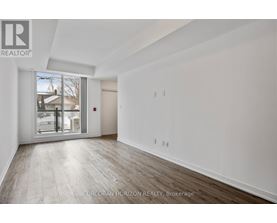 A spacious room with wood flooring and white walls, with a sliding glass door leading to a balcony.