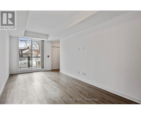 A spacious room with wood flooring and white walls, with a sliding glass door leading to a balcony.