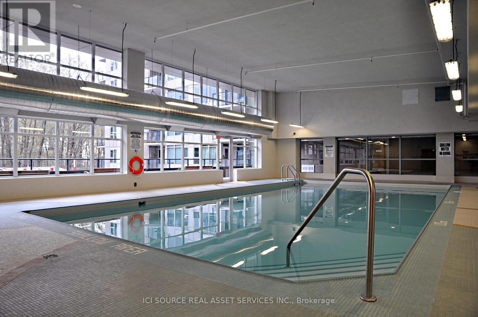 A large indoor swimming pool with a glass bottom and a metal ladder on the right side.