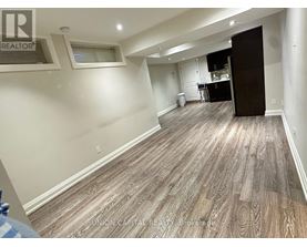 A spacious room with wood flooring and a kitchen area in the background.
