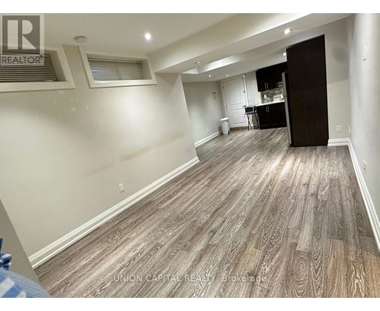 A spacious room with wood flooring and a kitchen area in the background.