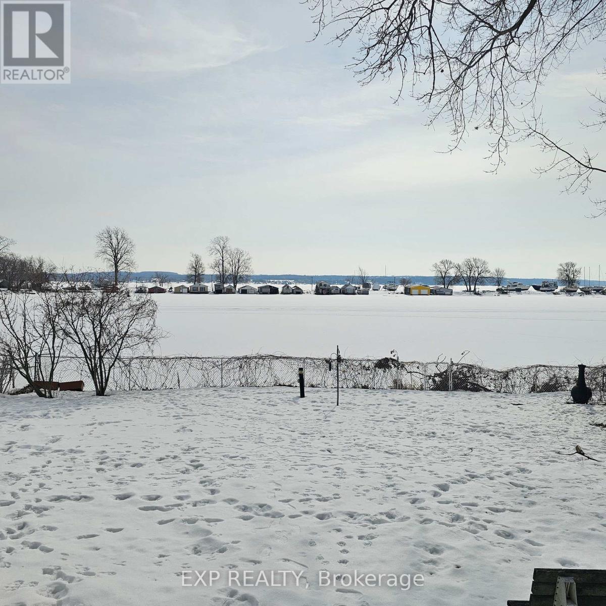 A snowy landscape with a body of water and leafless trees.