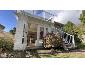 A small white house with a glass door and a staircase leading to the entrance.