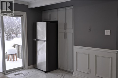 A kitchen with a refrigerator, cabinets, and a chair by a window.