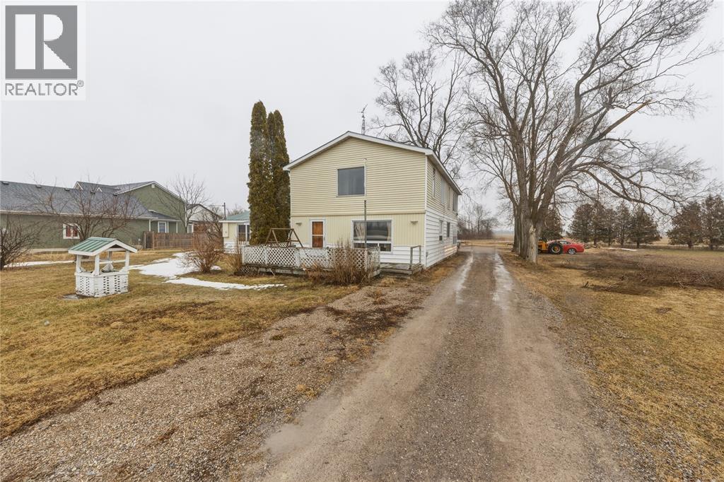 A gravel road leads to a white house with a yellow garage.