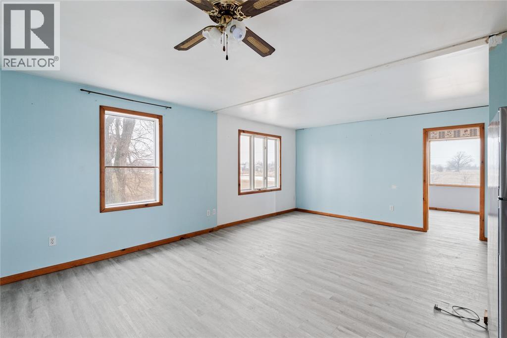 A spacious room with a ceiling fan and lighting, two windows, and a door.