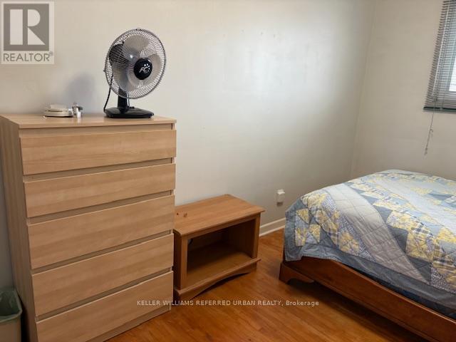 A bedroom with a bed, a fan, and a wooden dresser.