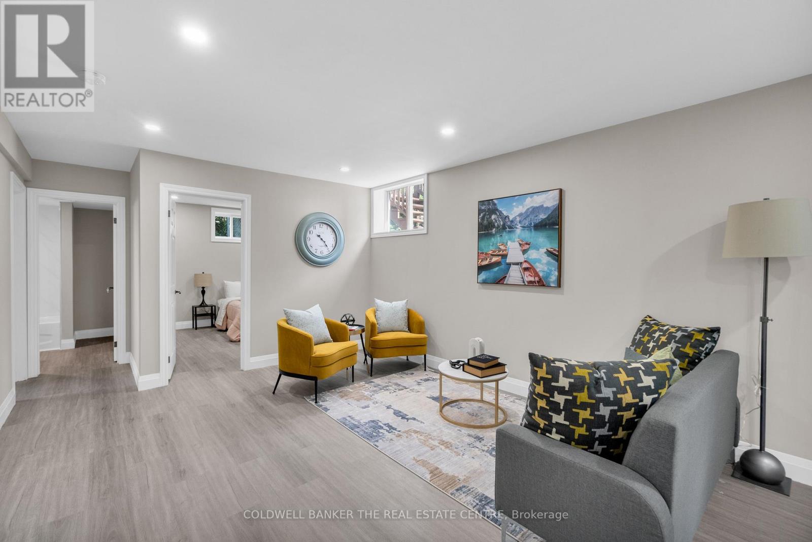 A living room with a grey couch, yellow chairs, and a painting on the wall.