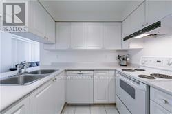 A white kitchen with a stove, sink, and cabinets.