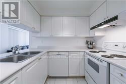 A white kitchen with a stove, sink, and cabinets.