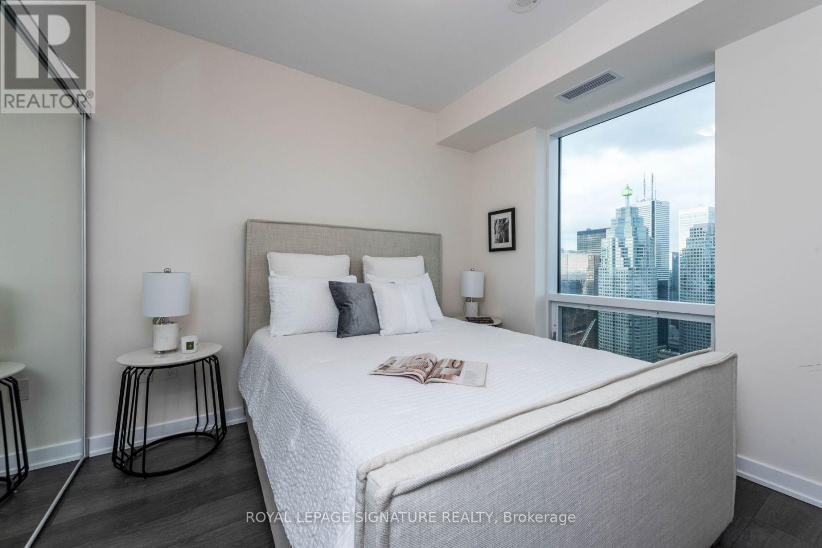 A bedroom with a large bed and a city view through the window.