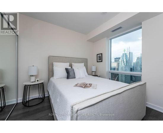 A bedroom with a large bed and a city view through the window.