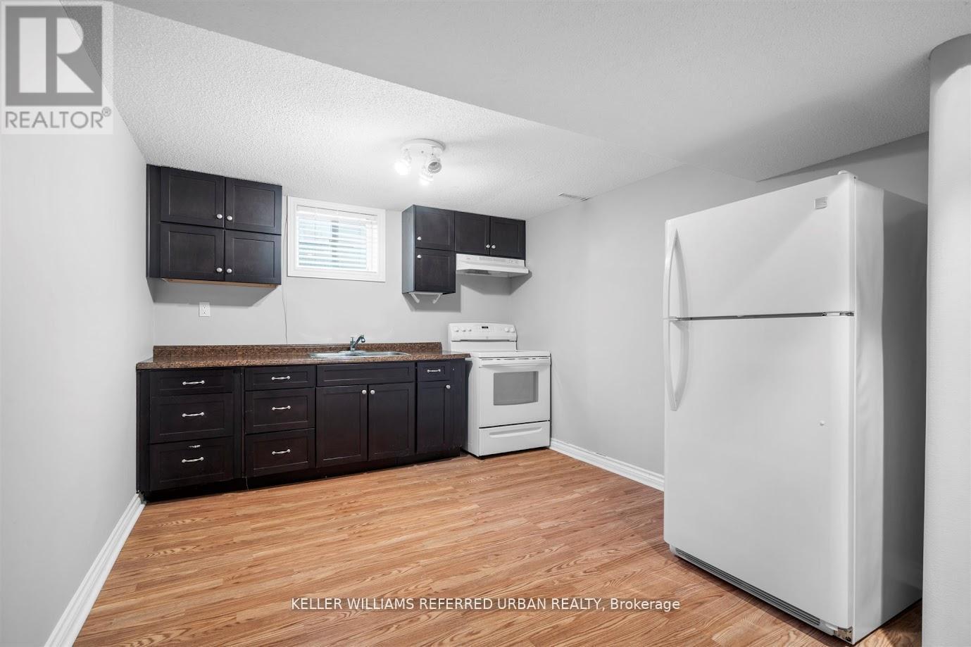 A kitchen with a white refrigerator, black cabinets, and a wooden floor.