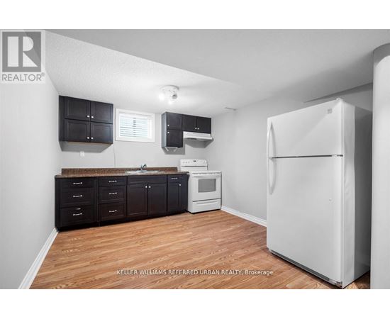 A kitchen with a white refrigerator, black cabinets, and a wooden floor.