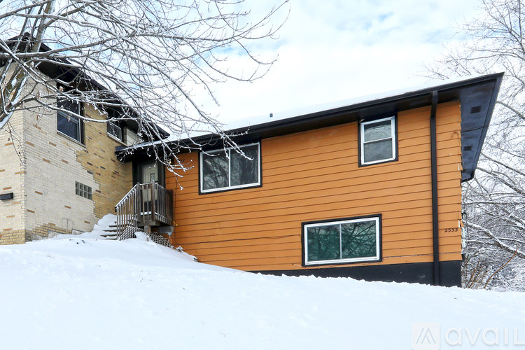 A house with a brown exterior and a black roof is surrounded by snow.