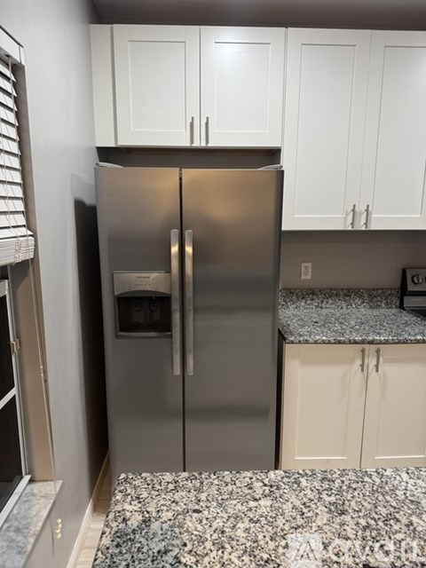A stainless steel refrigerator with a water and ice dispenser in the middle of the door stands in a kitchen with white cabinets.