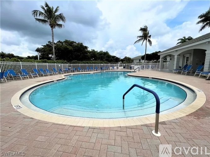 A round swimming pool surrounded by a brick patio and palm trees.