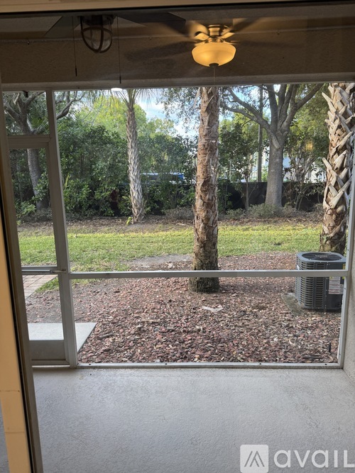 A patio with a fan and a view of trees and a lawn.
