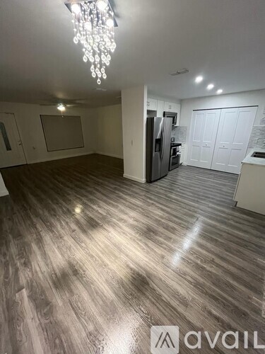 A spacious room with a chandelier and a kitchen area with white cabinets.