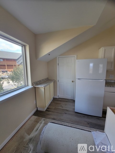 A kitchen with a white refrigerator and a window with a view of a parking lot.