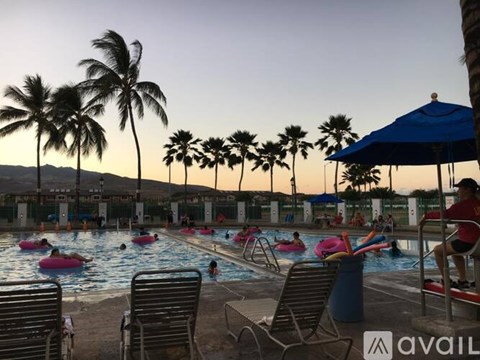 A pool with people swimming and relaxing under a blue umbrella.