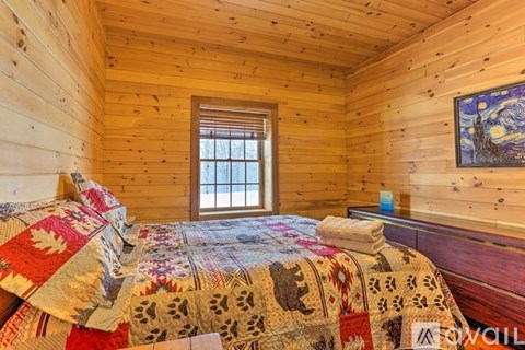 A bedroom with a bed covered in a quilt and a painting on the wall.