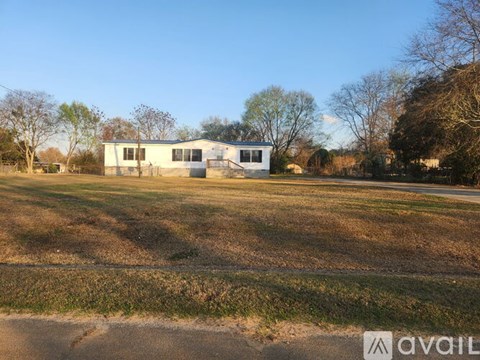 A house is situated in a field with trees in the background.