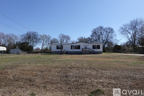 A white house is situated in a field with trees in the background.