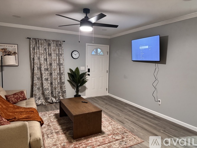 A living room with a couch, a coffee table, a ceiling fan, and a flat-screen TV mounted on the wall.