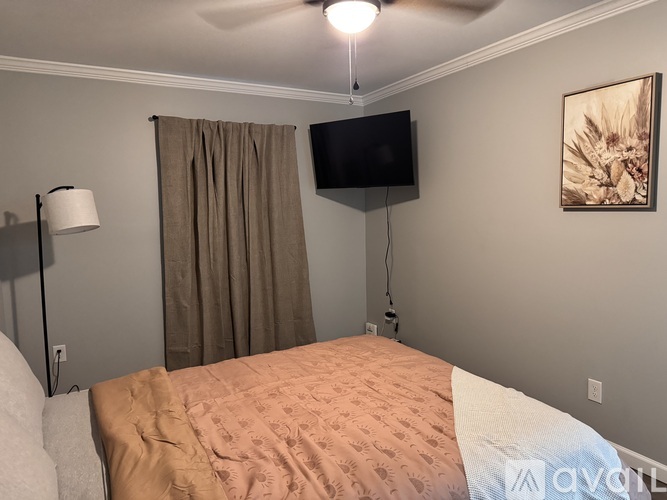 A bedroom with a bed, a lamp, a television, and a painting on the wall.