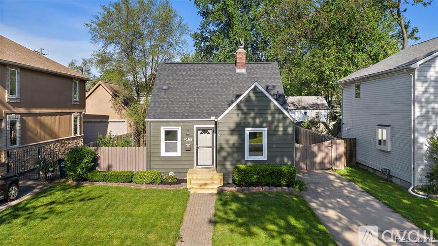 A small house with a grey roof and a white door is surrounded by a green lawn.