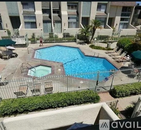 A large outdoor pool surrounded by a fence and lounge chairs.