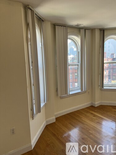 A room with wooden floors and three windows with curtains.