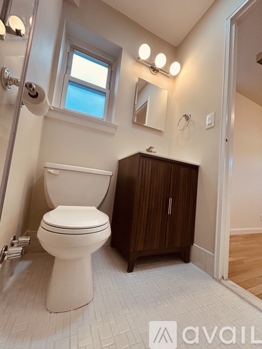 A white toilet in a bathroom with a wooden cabinet and a window.